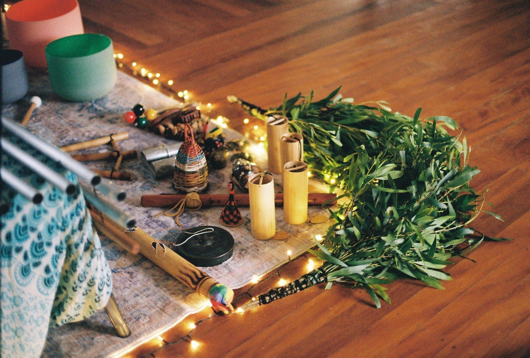 Gong, chimes, flutes and candles laid out on a rug with fresh greenery, ready for a sound journey
